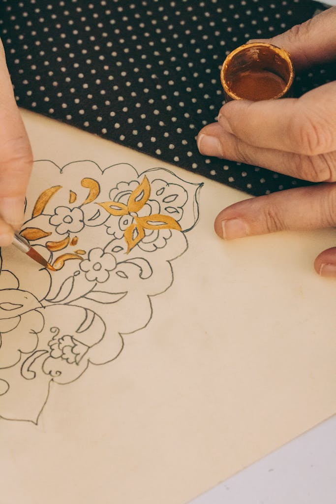 Close-up of a hand painting a floral batik design on fabric with natural dyes.