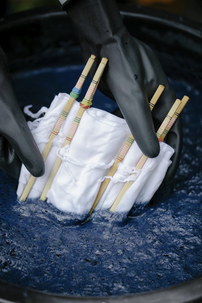 Detailed view of shibori textile dyeing, showing gloved hands submerging cloth in blue dye.