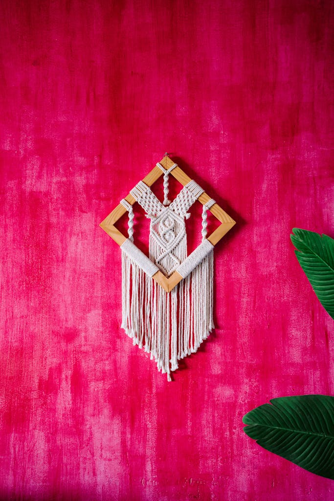 Handmade macrame art with wooden frame against a textured pink wall.