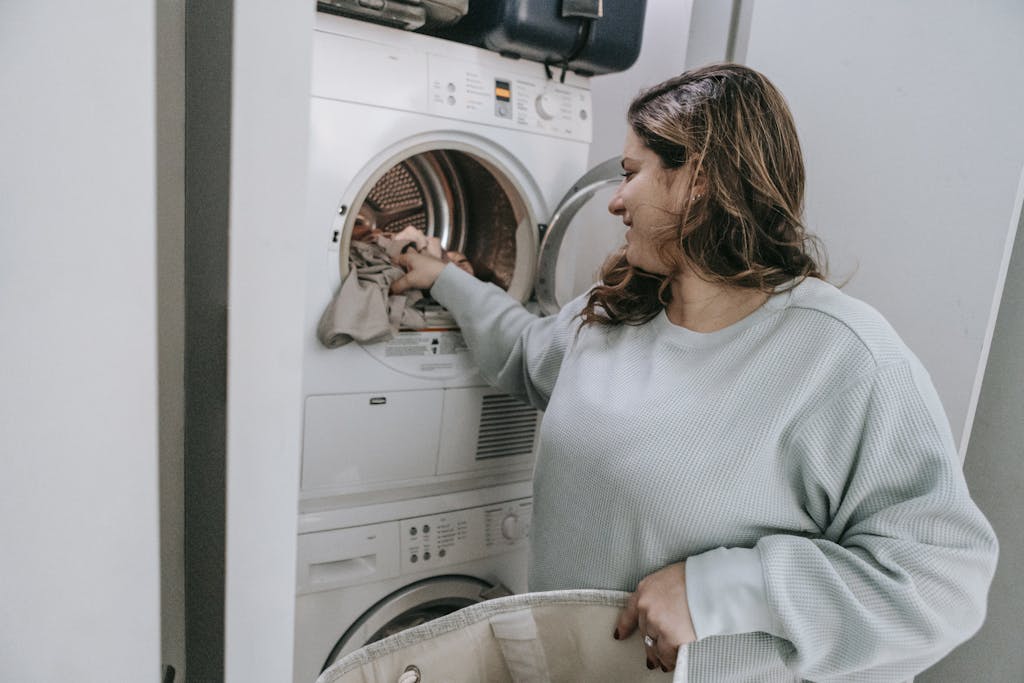 A woman loading clothes into a washing machine in a household setting.
